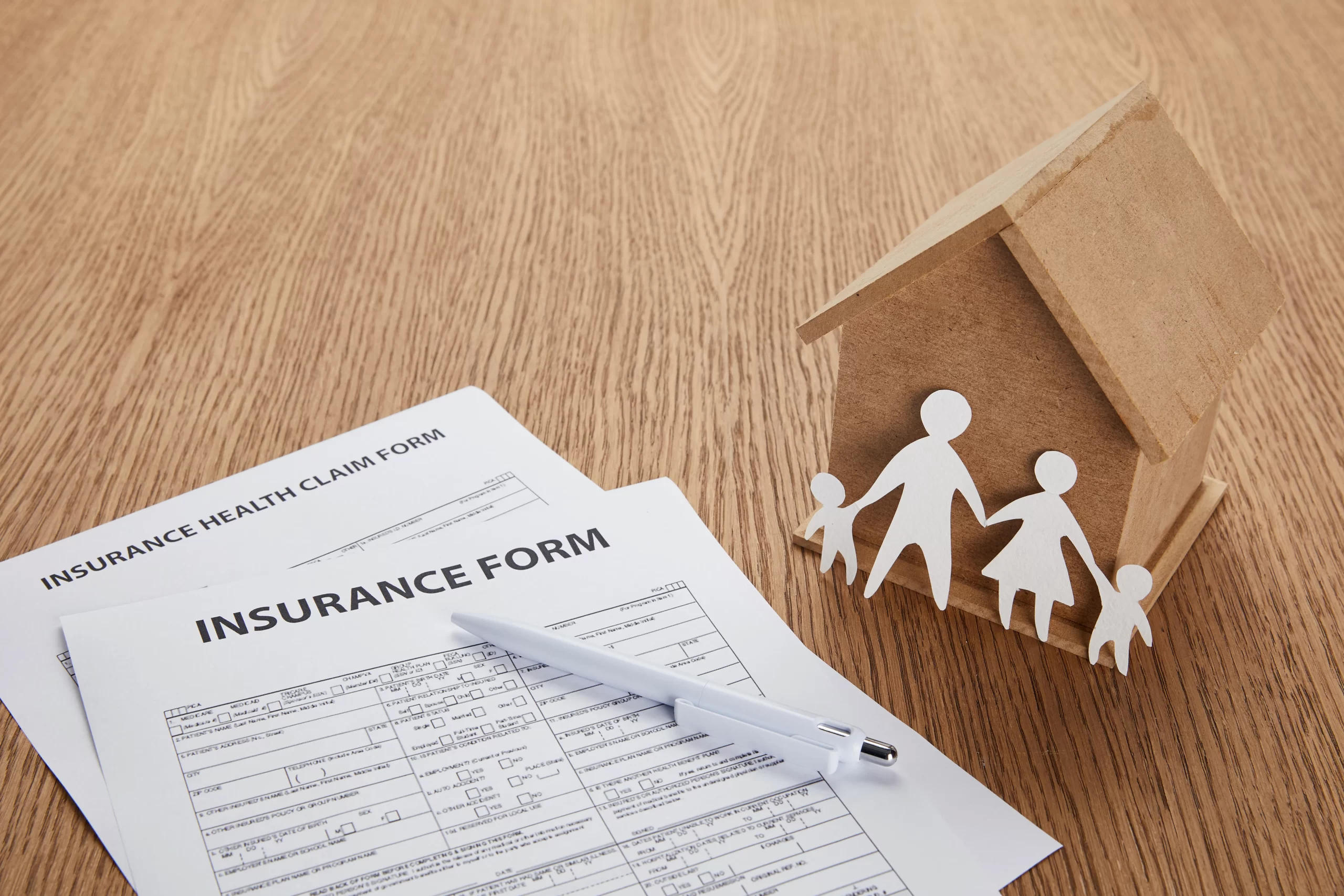 Close up view of insurance form beside a mini wooden house model.