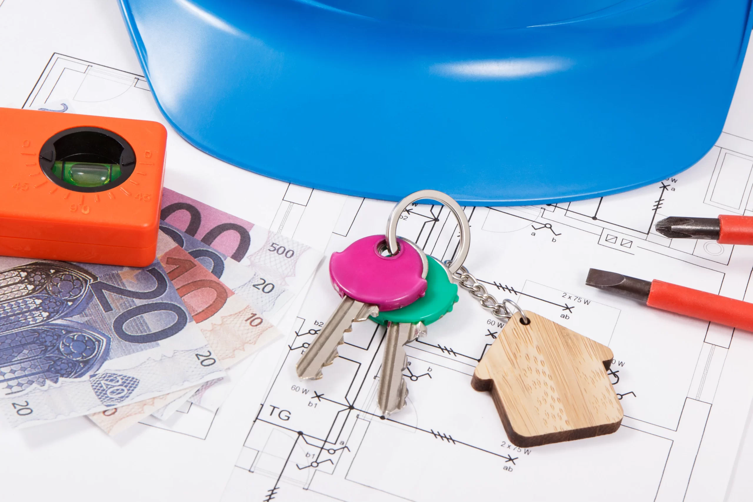 Keys with a house keychain beside a pile of cash on top of blueprints.