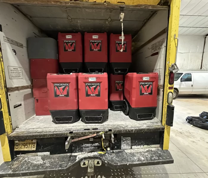 A truck's cargo area filled with stacked red Phoenix drying equipment, set against a backdrop of a clean workspace.