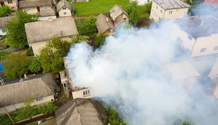 An aerial view of a house on fire with orange flames and white smoke.