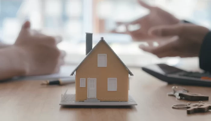 Close up house model on blurred background of real estate agent and client.