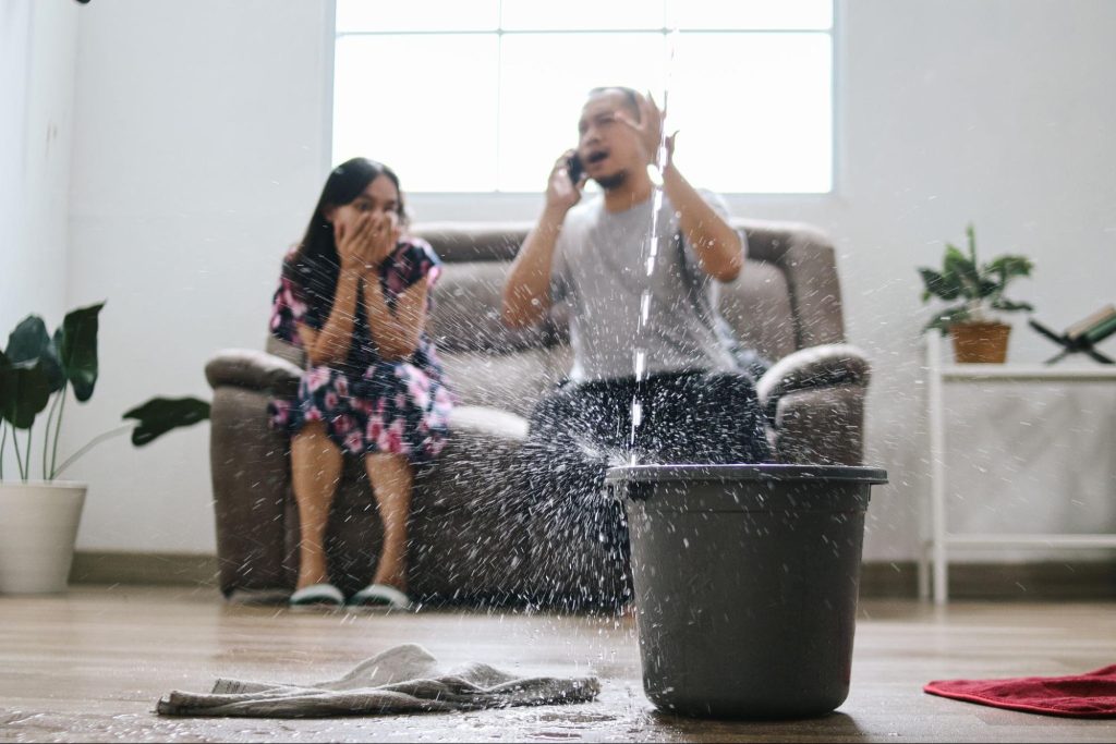 Frustrated wife watches as her husband calls a water damage company for urgent help with a leaking roof.